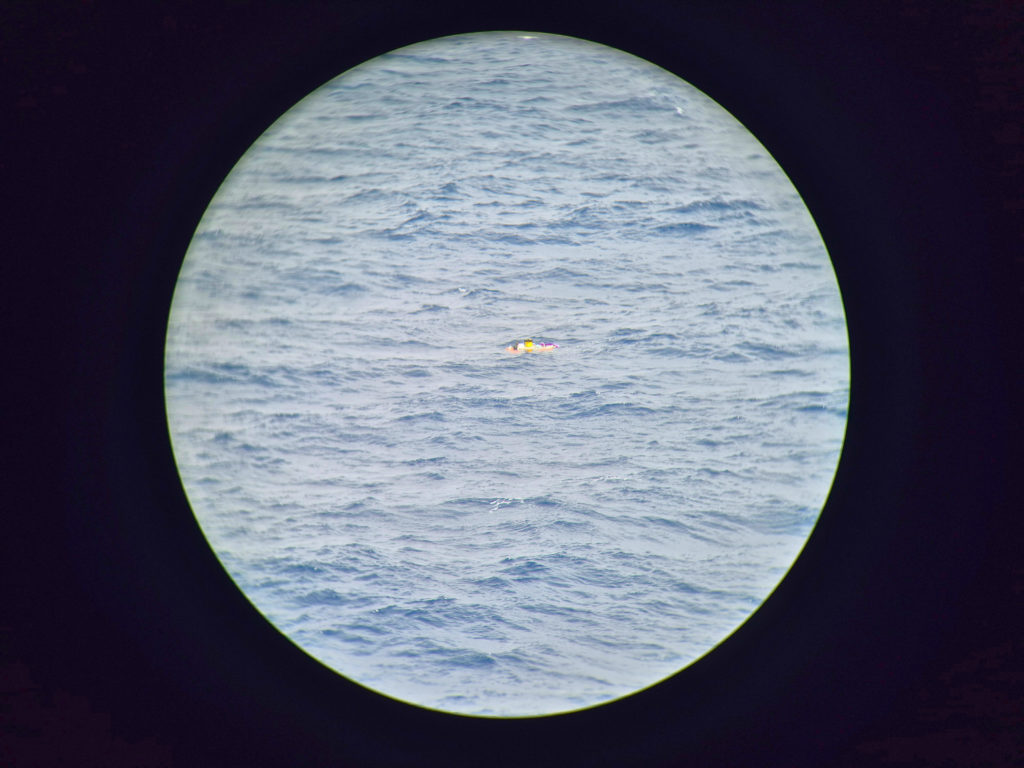 View through binoculars of a small floating ocean instrument visible in the distance on choppy water.