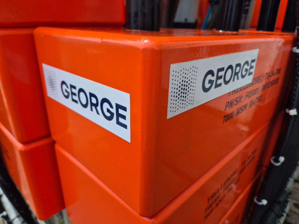 Close-up of bright orange blocks labeled ‘GEORGE’ on a marine scientific instrument aboard a research vessel.